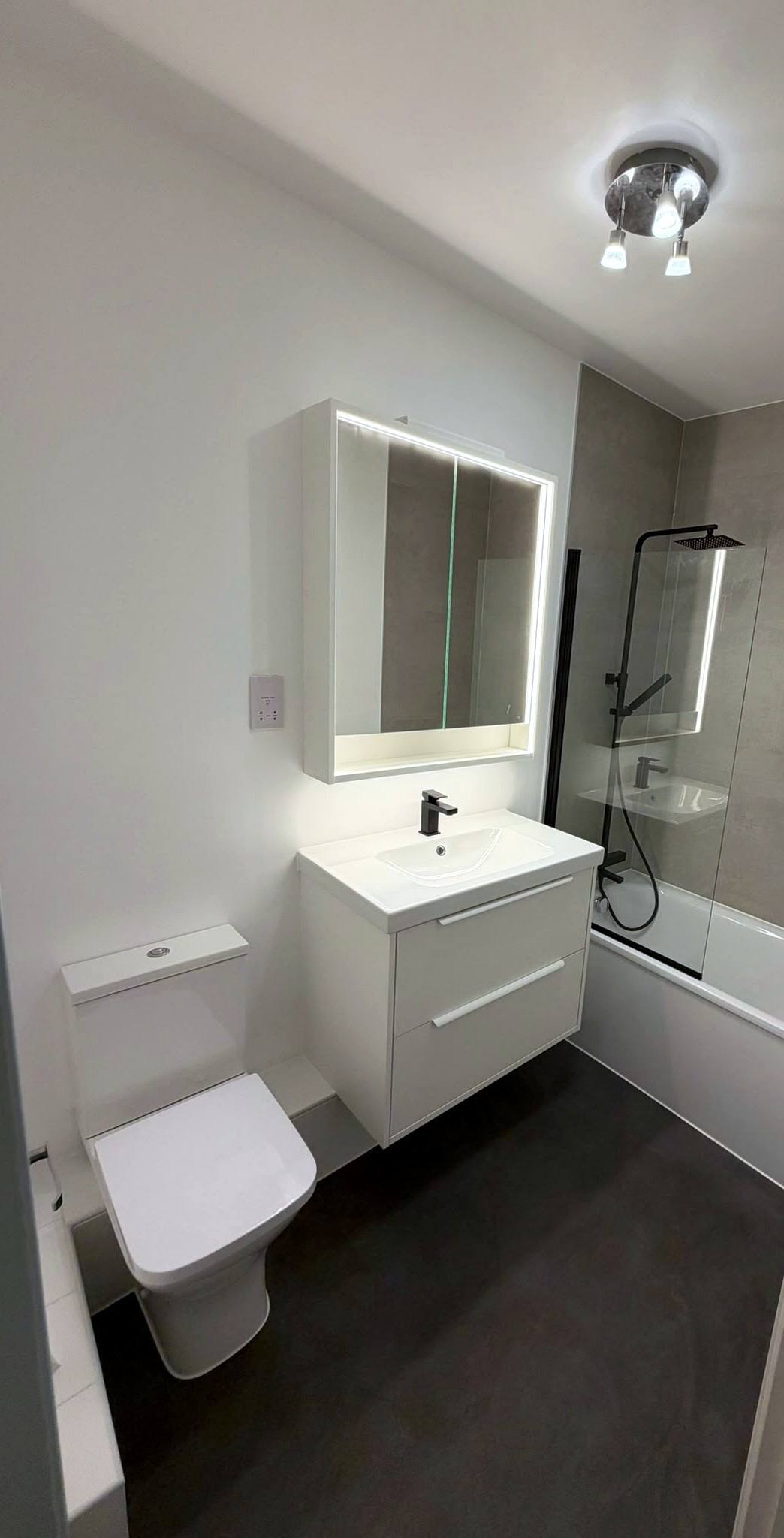 Bathroom with wall-hung vanity, illuminated mirror cabinet and shower over the bath
